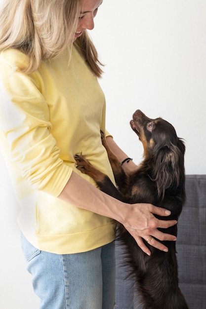 Joven mujer rubia en suéter amarillo mantenga gracioso terrier de juguete ruso marrón. Concepto de cuidado de mascotas.