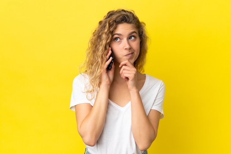Foto joven mujer rubia con teléfono móvil aislado sobre fondo amarillo y mirando hacia arriba