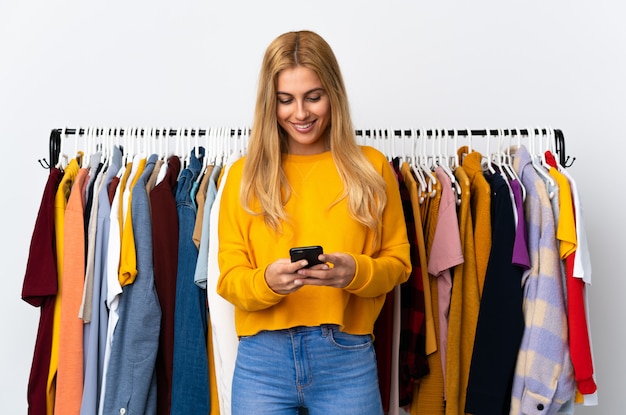 Foto joven mujer rubia uruguaya en una tienda de ropa enviando un mensaje con el móvil