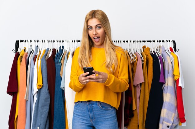 Joven mujer rubia uruguaya en una tienda de ropa sorprendida y enviando un mensaje