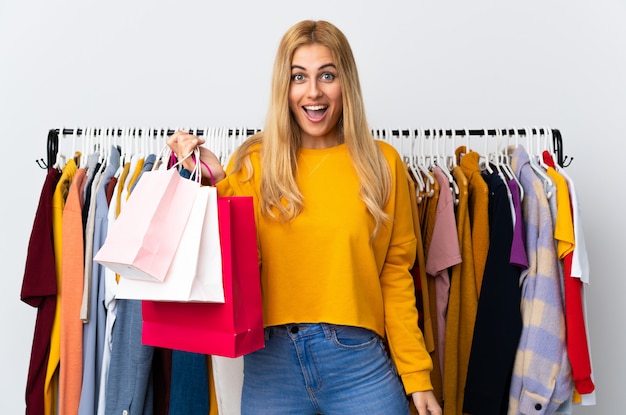 Joven mujer rubia uruguaya en una tienda de ropa y sosteniendo bolsas de compras con sorpresa y expresión facial conmocionada