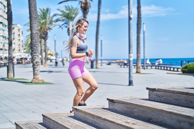 Joven mujer rubia vistiendo ropa deportiva corriendo en la playa