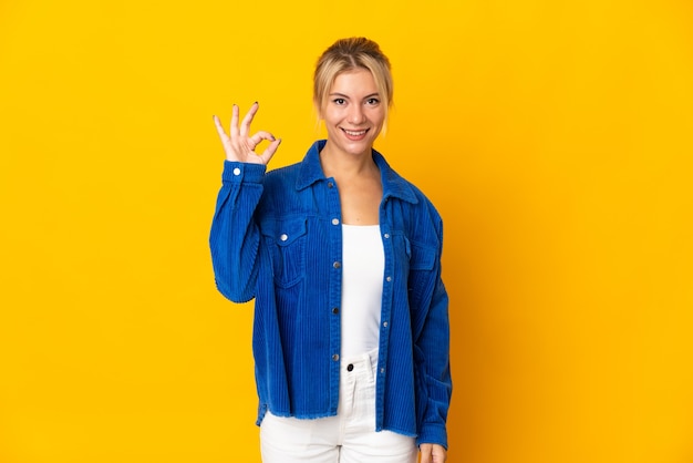 Joven mujer rusa aislada sobre fondo amarillo mostrando el signo de ok con los dedos