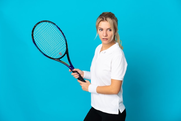 Joven mujer rusa aislada sobre fondo azul jugando al tenis