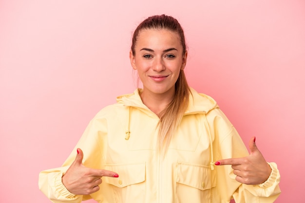 Joven mujer rusa aislada sobre fondo rosa persona apuntando con la mano a un espacio de copia de camisa, orgulloso y seguro