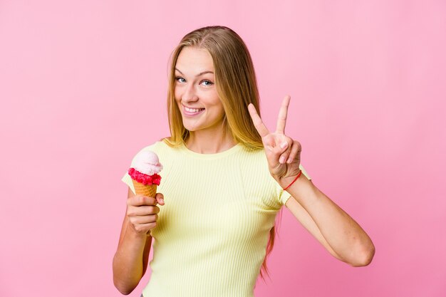 Foto joven mujer rusa comiendo un helado aislado mostrando el signo de la victoria y sonriendo ampliamente.