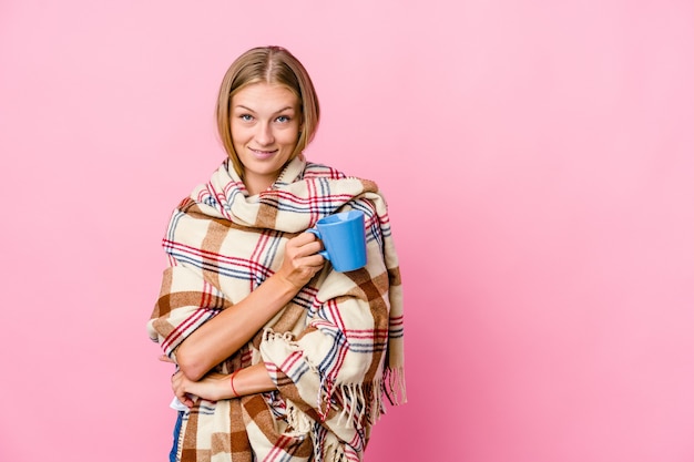 Joven mujer rusa envuelta en una manta bebiendo café sonriendo confiada con los brazos cruzados.