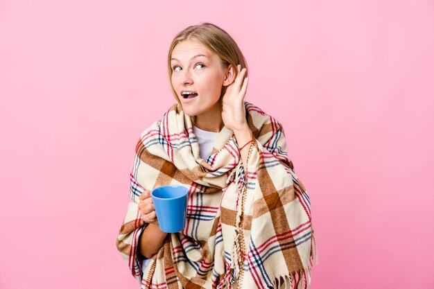 Joven mujer rusa envuelta en una manta tomando café tratando de escuchar un chisme.