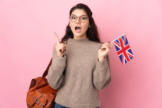 Joven mujer rusa sosteniendo una bandera del Reino Unido aislada en la pared rosa pensando en una idea apuntando con el dedo hacia arriba