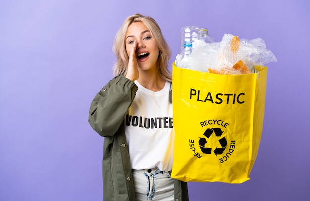 Joven mujer rusa sosteniendo una bolsa de reciclaje llena de papel para reciclar aislado en la pared púrpura gritando con la boca abierta