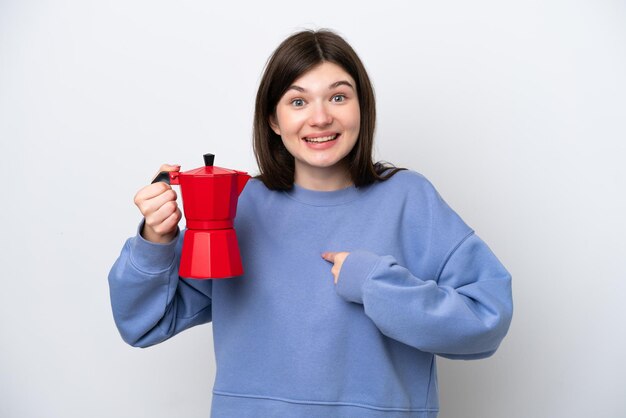 Joven mujer rusa sosteniendo una cafetera aislada de fondo blanco con una expresión facial sorpresa