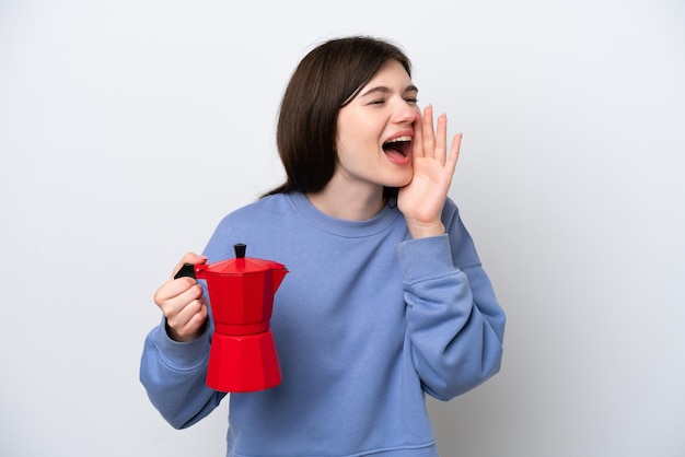 Joven mujer rusa sosteniendo una cafetera aislada de fondo blanco gritando con la boca abierta a un lado