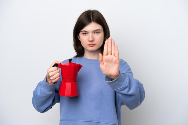 Joven mujer rusa sosteniendo una cafetera aislada de fondo blanco haciendo un gesto de parada