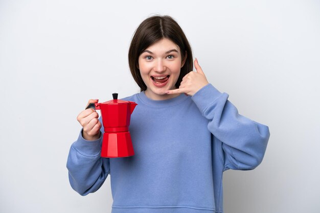 Joven mujer rusa sosteniendo una cafetera aislada de fondo blanco haciendo gestos telefónicos Llámame de nuevo