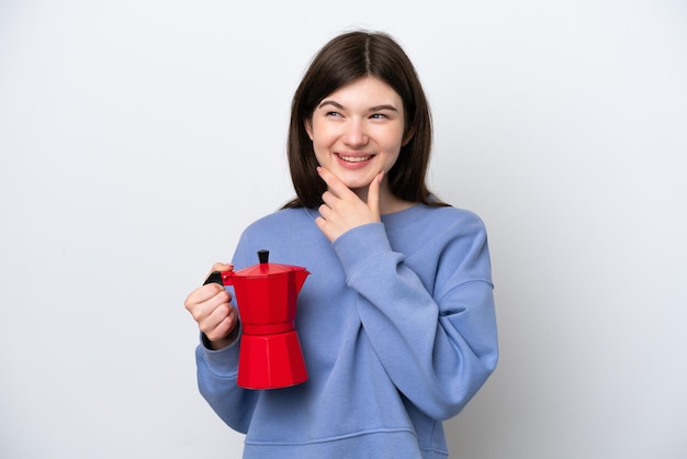 Joven mujer rusa sosteniendo una cafetera aislada de fondo blanco mirando hacia un lado y sonriendo