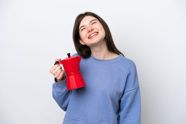 Joven mujer rusa sosteniendo una cafetera aislada de fondo blanco riéndose