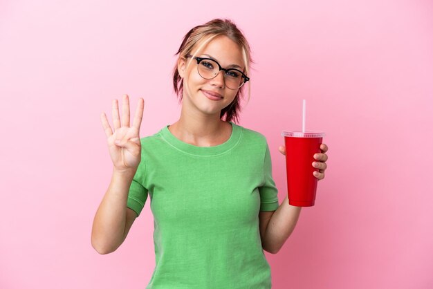 Joven mujer rusa sosteniendo un refresco aislado sobre fondo rosa feliz y contando cuatro con los dedos