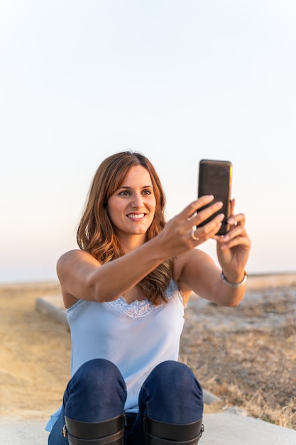 Joven mujer sentada en una escalera haciendo un selfie con su teléfono móvil.