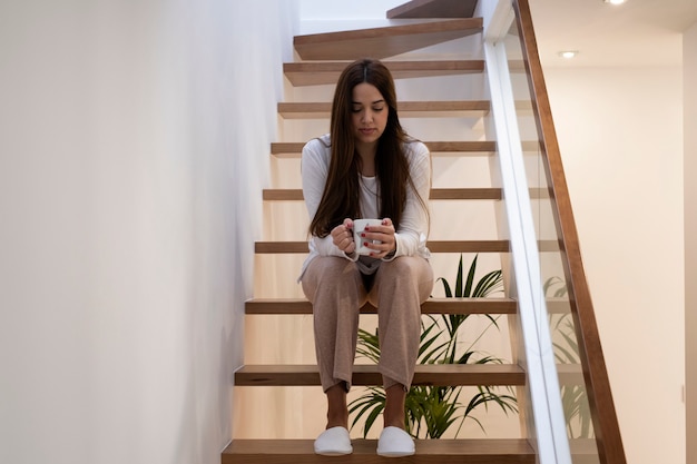 Foto joven mujer sentada en una escalera interior con una taza de café