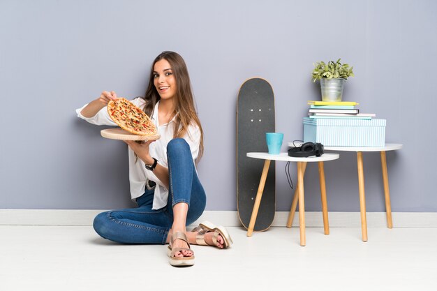 Joven mujer sentada en el piso con una pizza