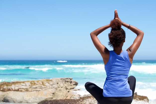 Joven mujer sentada en la playa en pose de yoga