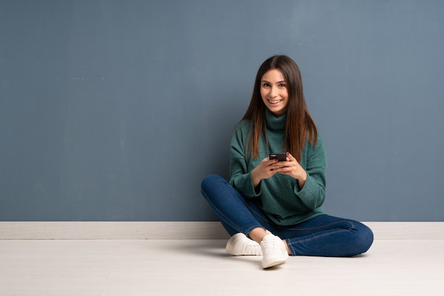 Joven mujer sentada en el suelo enviando un mensaje con el móvil