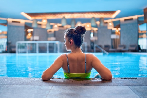 Joven mujer serena relajándose y relajándose sola en el agua de la piscina en el centro de fitness spa Salud mental y escapada