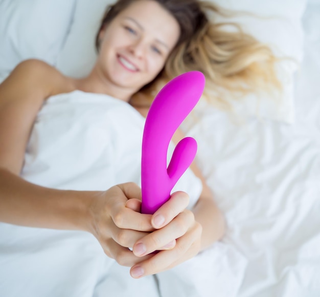 Joven mujer sexy en la cama sosteniendo en sus manos un juguete sexual para adultos