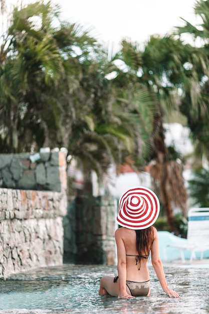 Joven mujer sexy disfrutando de descanso al borde de la piscina al aire libre