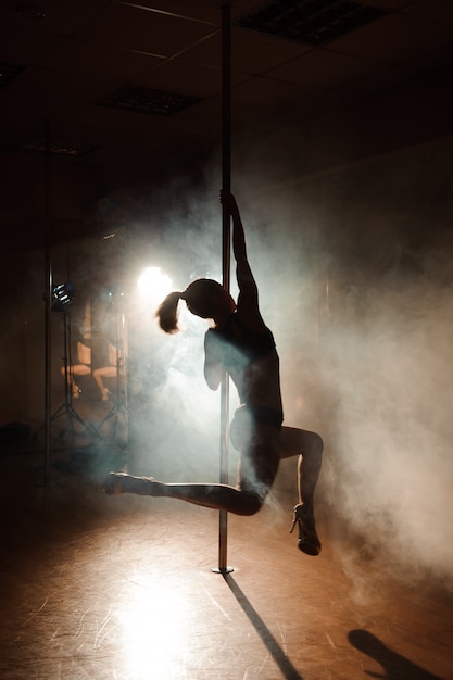 Joven mujer sexy ejercicio pole dance sobre un fondo oscuro