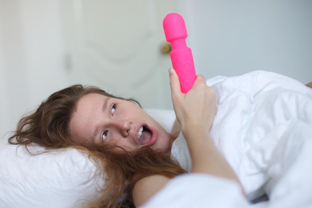 Joven mujer sexy feliz sostenga en la mano juguete sexual masturbarse con vibrador en la cama en el dormitorio en casa