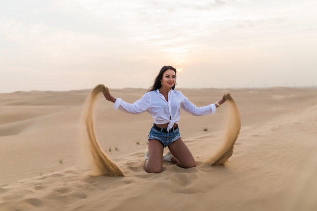 Joven mujer sexy jugando con arena en el desierto de dunas.