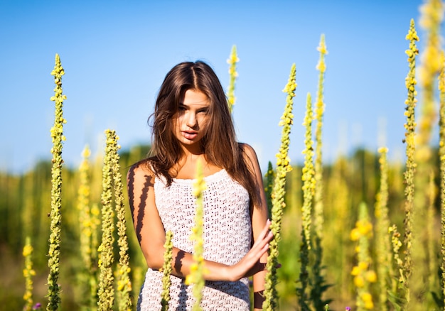 Joven mujer sexy en mini vestido blanco de pie con los ojos cerrados y disfrutando del sol