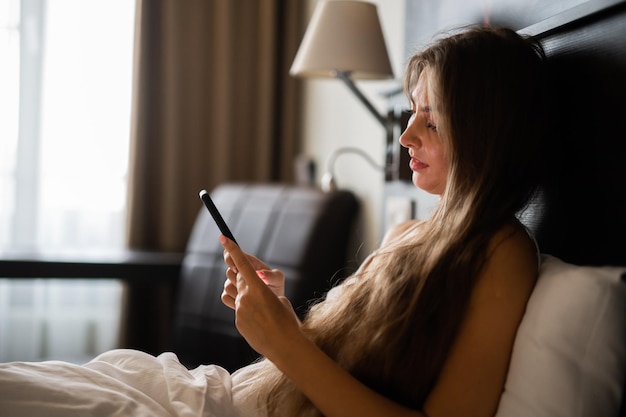 Joven mujer sexy relajante con su teléfono inteligente en su cama