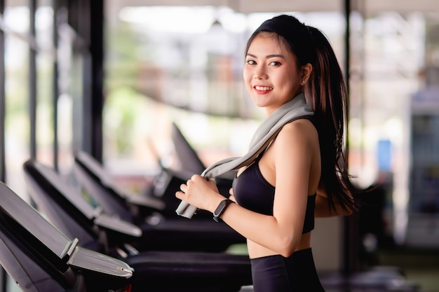 Joven mujer sexy con ropa deportiva, tela a prueba de sudor y reloj  inteligente usa toalla para limpiar el sudor durante el entrenamiento en el  gimnasio moderno, sonrisa, espacio de copia