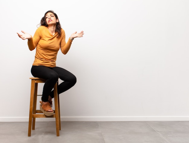 Foto joven mujer sintiéndose estupefacta, sentada en una silla junto a copyspace