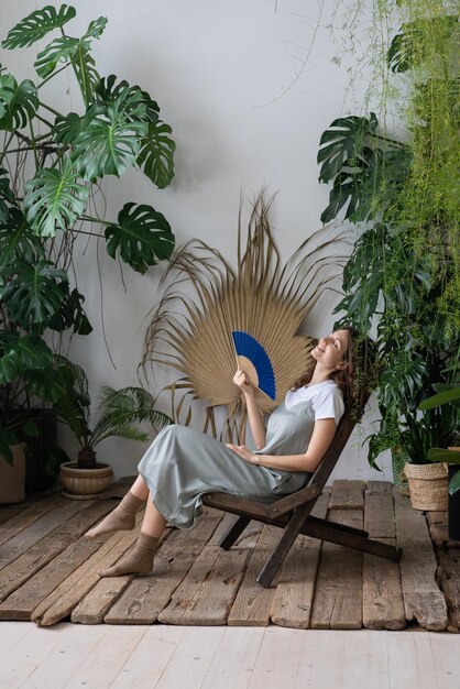 Joven mujer soñadora y relajada que usa un abanico de papel mientras se relaja en un hermoso y refrescante jardín casero