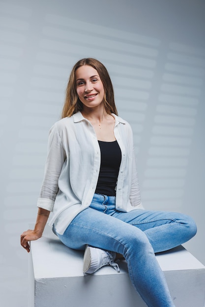 Joven mujer sonriente con una camisa blanca, camiseta negra y jeans sobre un fondo gris Retrato de una mujer morena con una sonrisa en la cara