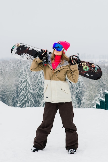 Joven mujer sonriente deportiva en invierno con snowboard, gafas