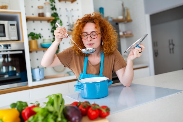 Joven mujer sonriente disfrutando del sabor y el olfato mientras prepara el almuerzo en la cocina