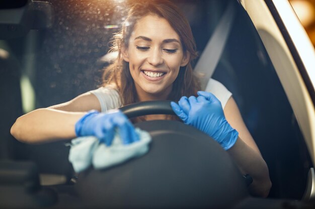 Una joven mujer sonriente con guantes protectores en las manos limpia un volante con un paño listo para salir a la carretera.