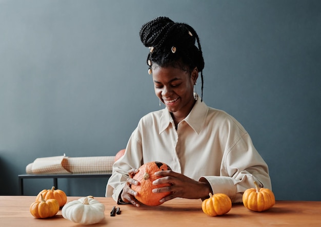 Joven mujer sonriente mirando una cara espeluznante en una calabaza madura de Halloween