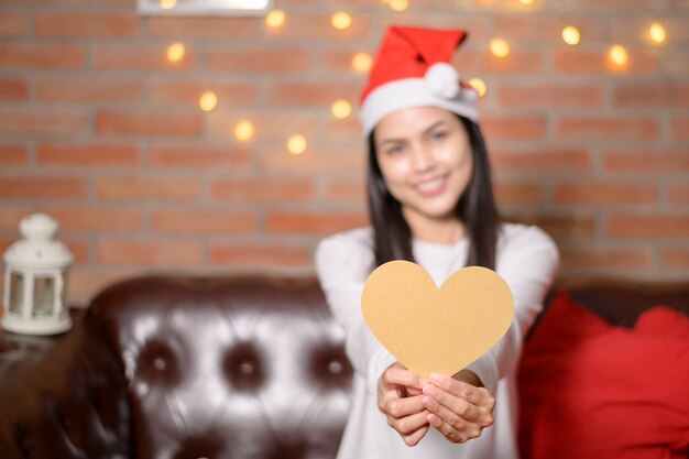 Una joven mujer sonriente con sombrero rojo de Santa Claus mostrando un modelo en forma de corazón el día de Navidad, concepto de vacaciones.