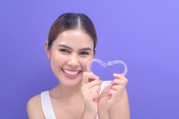 Una joven mujer sonriente sosteniendo aparatos invisalign en estudio, salud dental y concepto de ortodoncia.