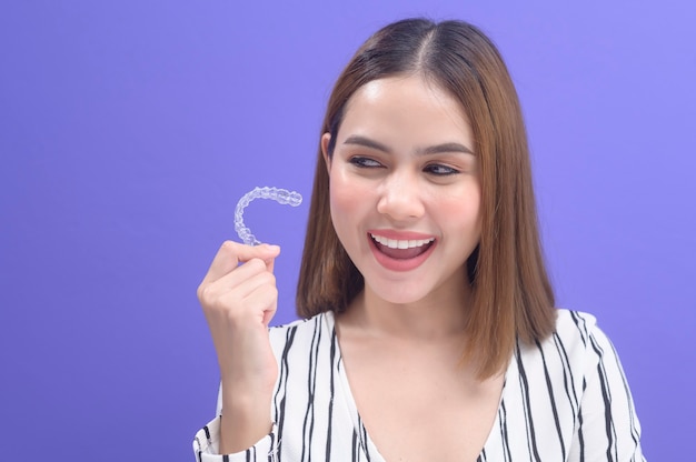 Una joven mujer sonriente sosteniendo aparatos invisalign en estudio, salud dental y concepto de ortodoncia.