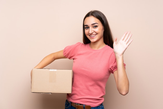 Joven mujer sosteniendo una caja para moverla a otro sitio y saludando