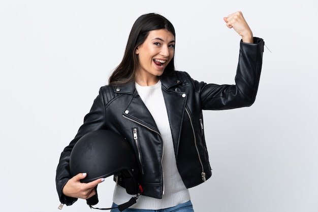 Joven mujer sosteniendo un casco de moto sobre pared blanca haciendo un gesto fuerte