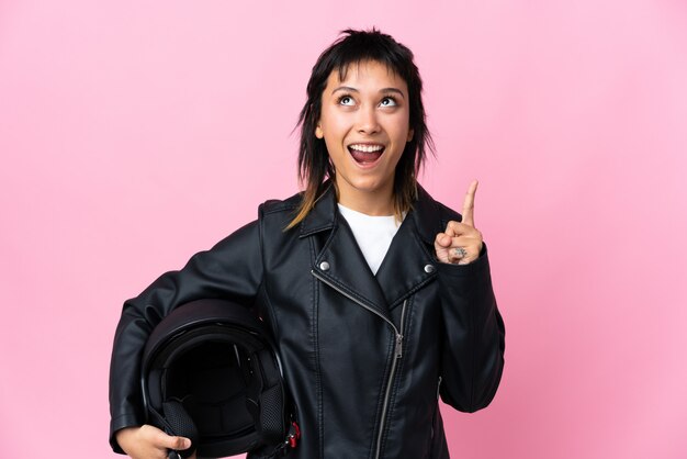 Joven mujer sosteniendo un casco de motocicleta sobre rosa aislado apuntando con el dedo índice una gran idea