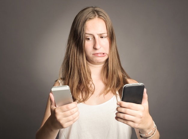 Joven mujer sosteniendo dos celulares en gris