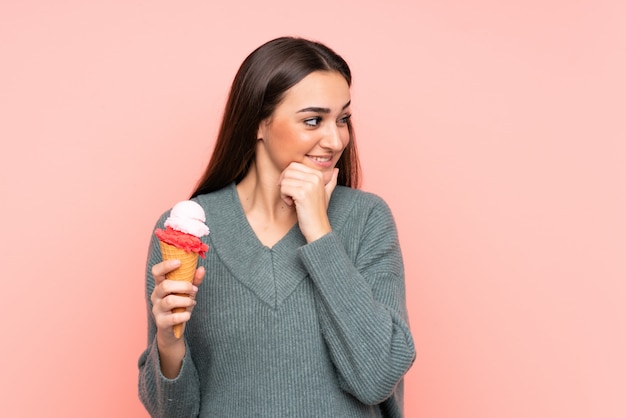 Joven mujer sosteniendo un helado de cucurucho aislado en rosa pensando en una idea y mirando de lado